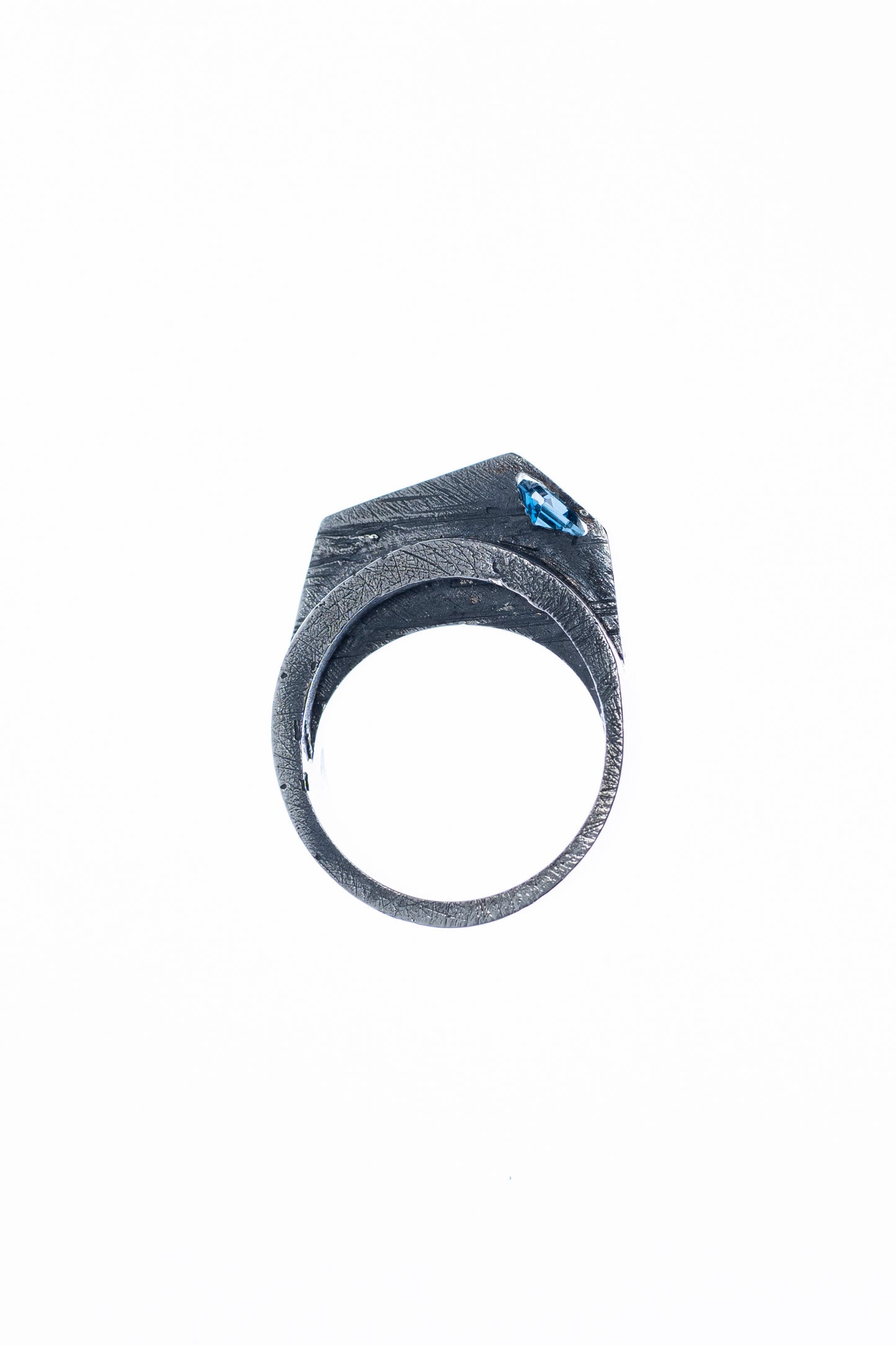 A close-up view of a silver statement ring showcasing its angular, textured design, with a London Blue Topaz stone set at an angle, highlighted against a soft, light background.