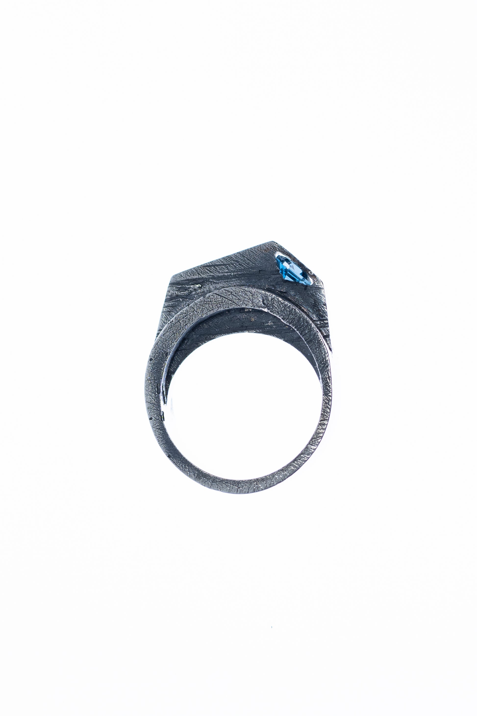 A close-up view of a silver statement ring showcasing its angular, textured design, with a London Blue Topaz stone set at an angle, highlighted against a soft, light background.